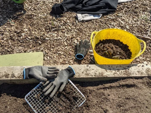 Bild von schwarzen Handschuhen und einem gelben Eimer mit Erde
